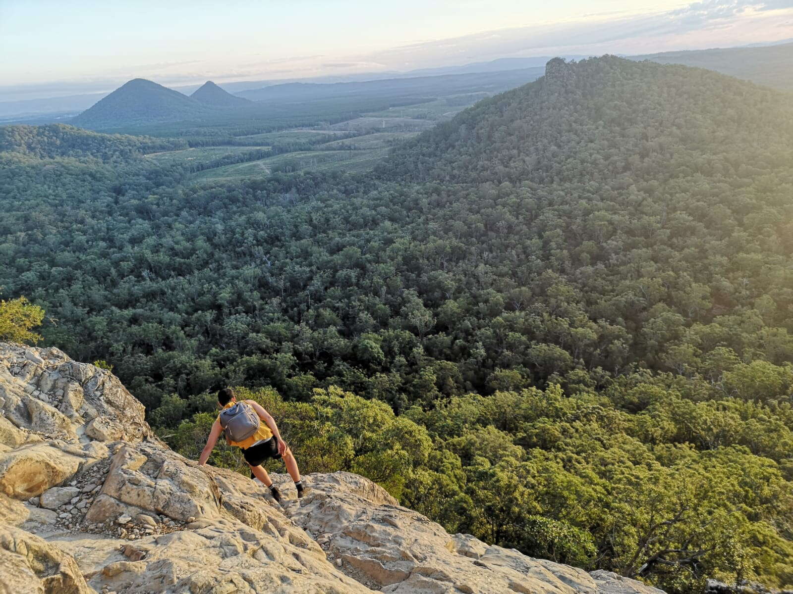 Hiker climbing a rocky ridge above forested hills in Australia
