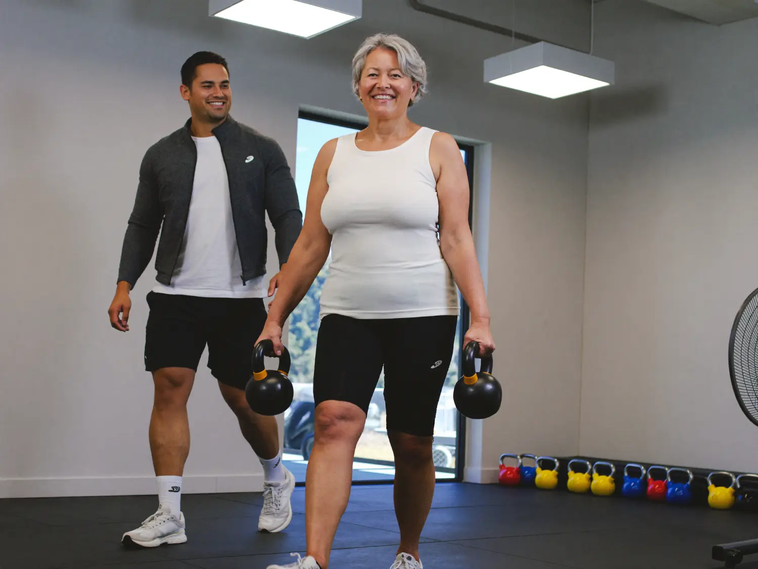 Trainer walking beside an older woman carrying two kettlebells